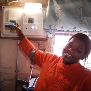 ‘n Vreugdevolle gestremde Bukelwa Mbuzweni by haar elektrisiteitstoestel vir elektrisiteit in haar woning